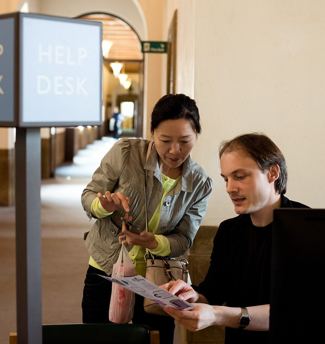 Librarian providing assistance to library user by pointing to written information in a leaflet 