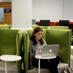 Person reading from laptop screen on a green chair in a library